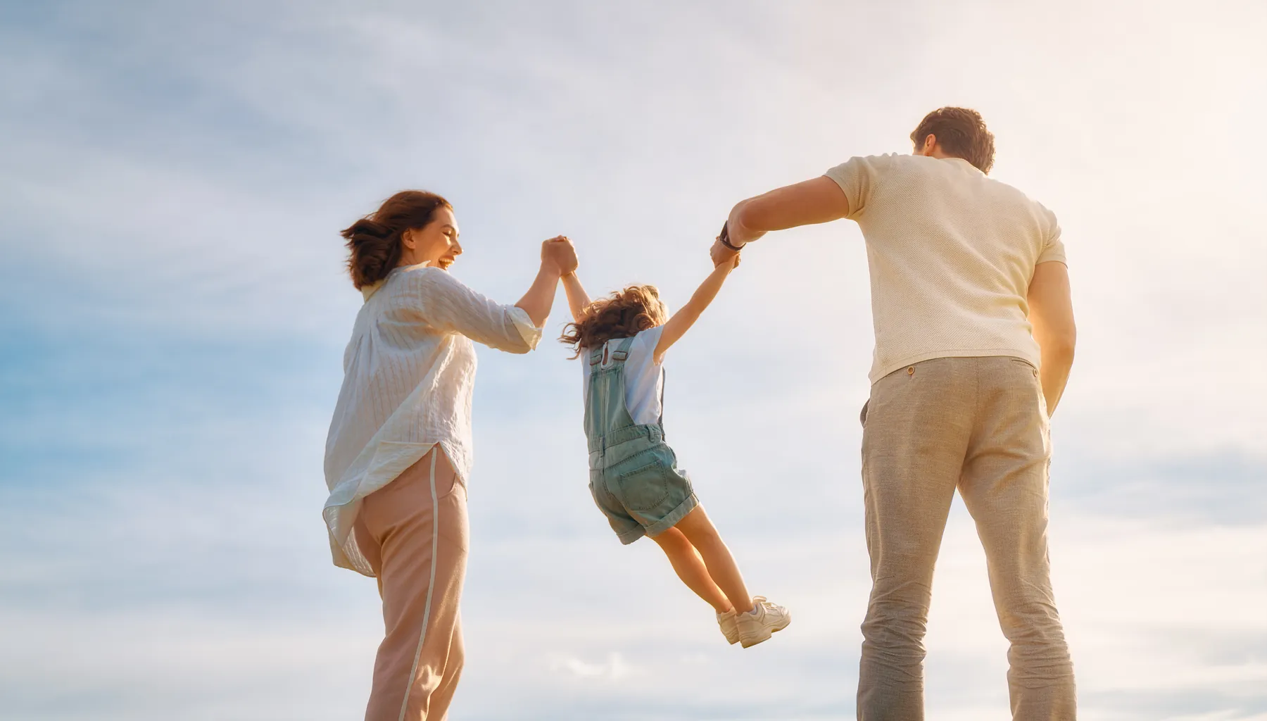 Dos padres levantando a su hija pequeña entre los dos al atardecer